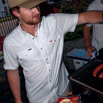 Man wearing The Stay Late white shirt grilling sausages outdoors in a backyard setting