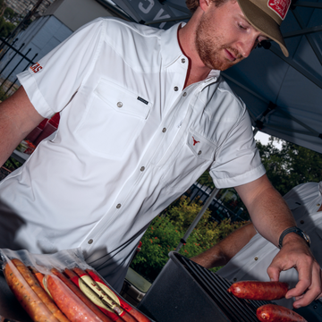 Man wearing The Stay Late white shirt grilling sausages outdoors in daylight