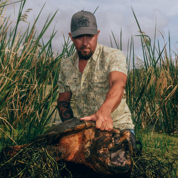 man holding large turtle wearing the swamp donkey shirt