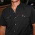 Close-up of a man wearing a black short-sleeve button-up shirt featuring The Tortilla logo on the chest pocket