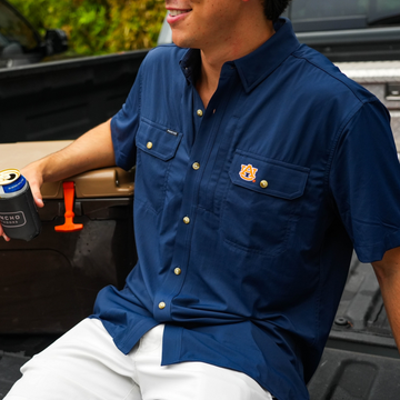 Man wearing The War Eagle navy blue outdoor shirt sitting in pickup bed holding can cooler outdoors