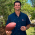Man wearing The War Eagle shirt holding a football outdoors surrounded by greenery