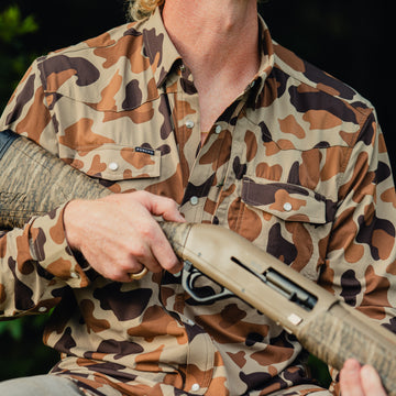 man holding shotgun wearing white wing shirt