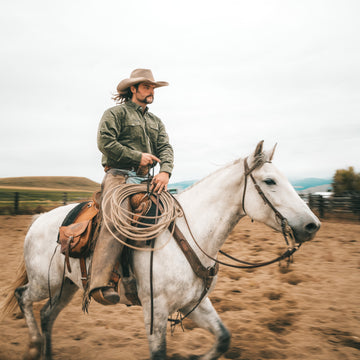 Man wearing The Zilker shirt riding a white horse outdoors