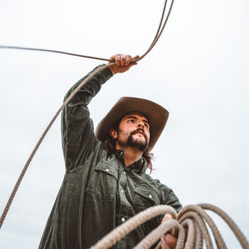 Man wearing The Zilker shirt outdoors holding a rope with a cowboy hat