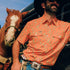Cowboy leaned up on horse trailer in The Bisbee shirt
