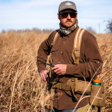 Man wearing The Clark brown outdoor shirt with backpack and cap in dry grass field