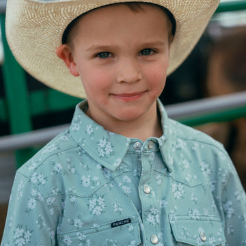Young boy wearing The Marty Robbins blue floral outdoor shirt and a straw hat outdoors