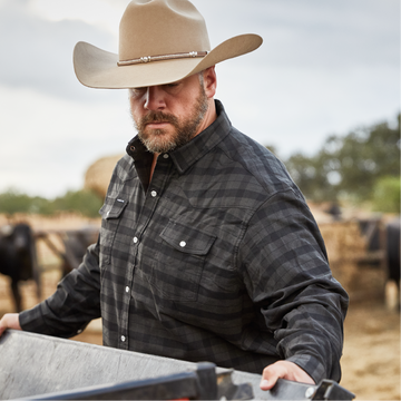man working with four wheeler on ranch in black and grey flannel