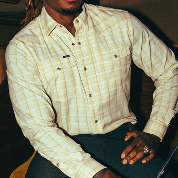 Man wearing The Yellowbelly yellow plaid outdoor shirt sitting with hand on knee