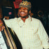 Man smiling wearing The Yellowbelly light yellow outdoor shirt and camo hat indoors