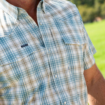 Close-up of a man wearing The Sandbar shirt with a green and white plaid pattern outdoors on a sunny day