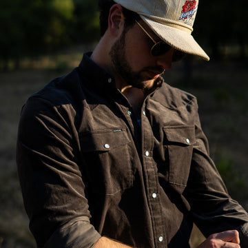 Man buttoning up black corduroy shirt outside