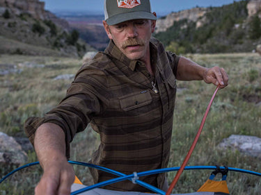 man pitching tent wearing green plaid flannel