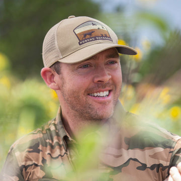 Smiling man wearing a tan Busted Covey Hat outdoors in a natural setting