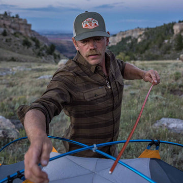 guy wearing flannel setting up tent